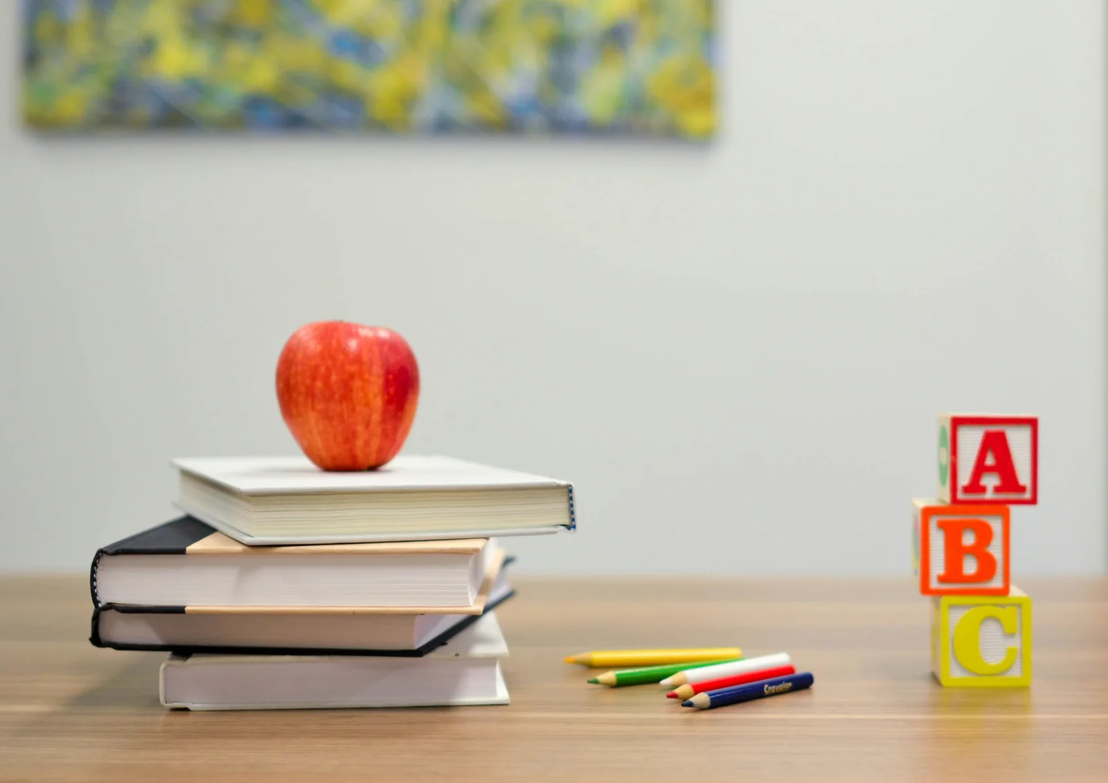 An apple on a stack of books beside alphabet blocks and coloured pencils